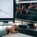 A trader analyzes Bitcoin charts on a computer screen with financial graphs in the background.