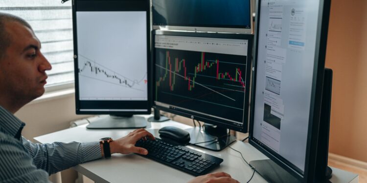 A trader analyzing cryptocurrency charts on multiple screens in a modern office environment.