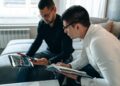 Two businessmen discussing finance with charts and crypto tokens in the background.
