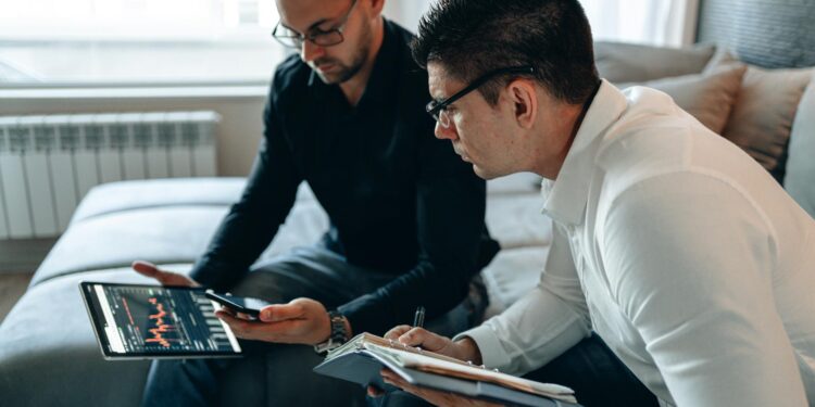 Two businessmen discussing finance with charts and crypto tokens in the background.