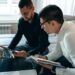 Two businessmen discussing finance with charts and crypto tokens in the background.