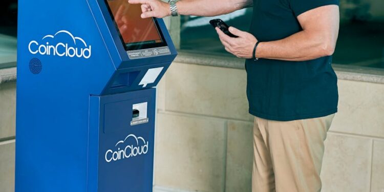 A crypto ATM in a public space with a warning sign about fraud risks.