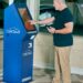 A crypto ATM in a public space with a warning sign about fraud risks.