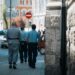 A handcuffed man being escorted by authorities outside a courthouse with Bitcoin symbols in the background.