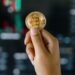 Person holding a Bitcoin Visa card amid cryptocurrency symbols and financial charts.