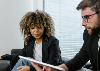 Two professionals discussing blockchain technology over laptops with financial graphs displayed.