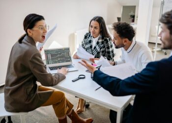 A group of employees in an office setting discussing financial strategies and layoffs.
