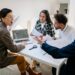 A group of employees in an office setting discussing financial strategies and layoffs.