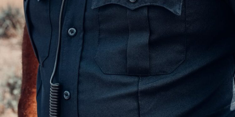 An ICE agent in uniform stands outside a building during a law enforcement operation.