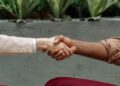 Two business professionals shake hands over a smartphone, symbolizing a strategic acquisition.
