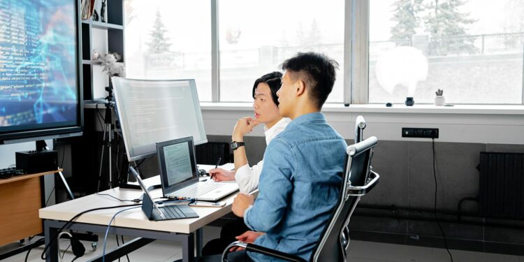 Developers collaborating on a Bitcoin project with code and digital screens in a tech workspace.