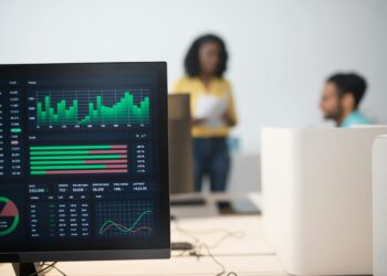 Oil trading floor with screens showing prices, traders discussing strategy in a busy environment.