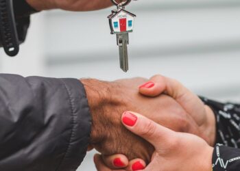 Hands shaking over a contract, cryptocurrency symbols in the background, symbolizing a real estate deal.