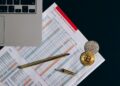 A Bitcoin coin alongside financial documents and a regulatory book on a desk.