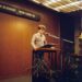 Jack Dorsey speaking at a podium with charts on AI and management behind him.