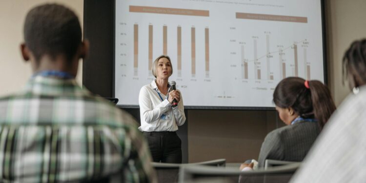 Stephanie Cutter speaking at a conference with financial graphs displayed in the background.