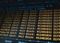 A computer screen displays blockchain code while Bitcoin symbols surround it.