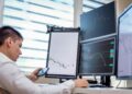 Traders analyzing stock charts with digital screens showcasing tokenized stocks and ETFs.