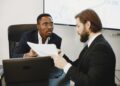 Two professionals discussing crypto payment solutions at a conference table with charts and laptops.