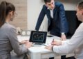 Crypto executives discuss banking charters at a conference table with financial charts and laptops.