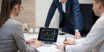 Crypto executives discuss banking charters at a conference table with financial charts and laptops.