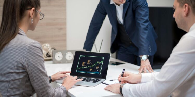 Crypto executives discuss banking charters at a conference table with financial charts and laptops.