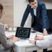 Crypto executives discuss banking charters at a conference table with financial charts and laptops.