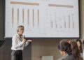 Peter Thiel speaking at a finance conference, with charts and graphs in the background.